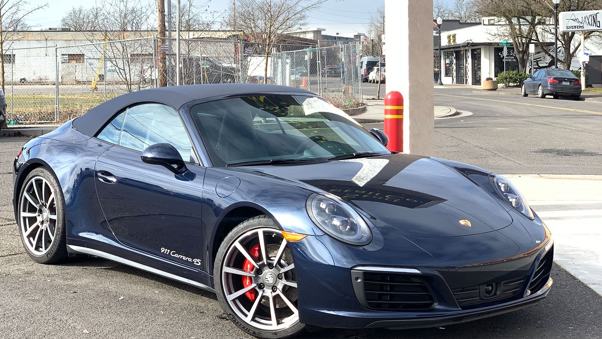 Blue Porsche convertible parked in front of a building, with red brake calipers.