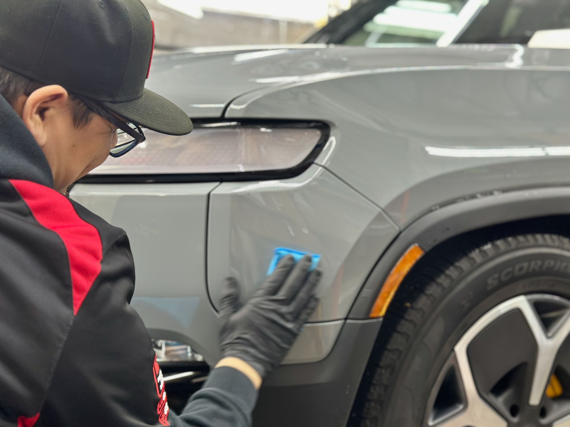Person in black gloves applying a blue pad to a gray car's side panel.