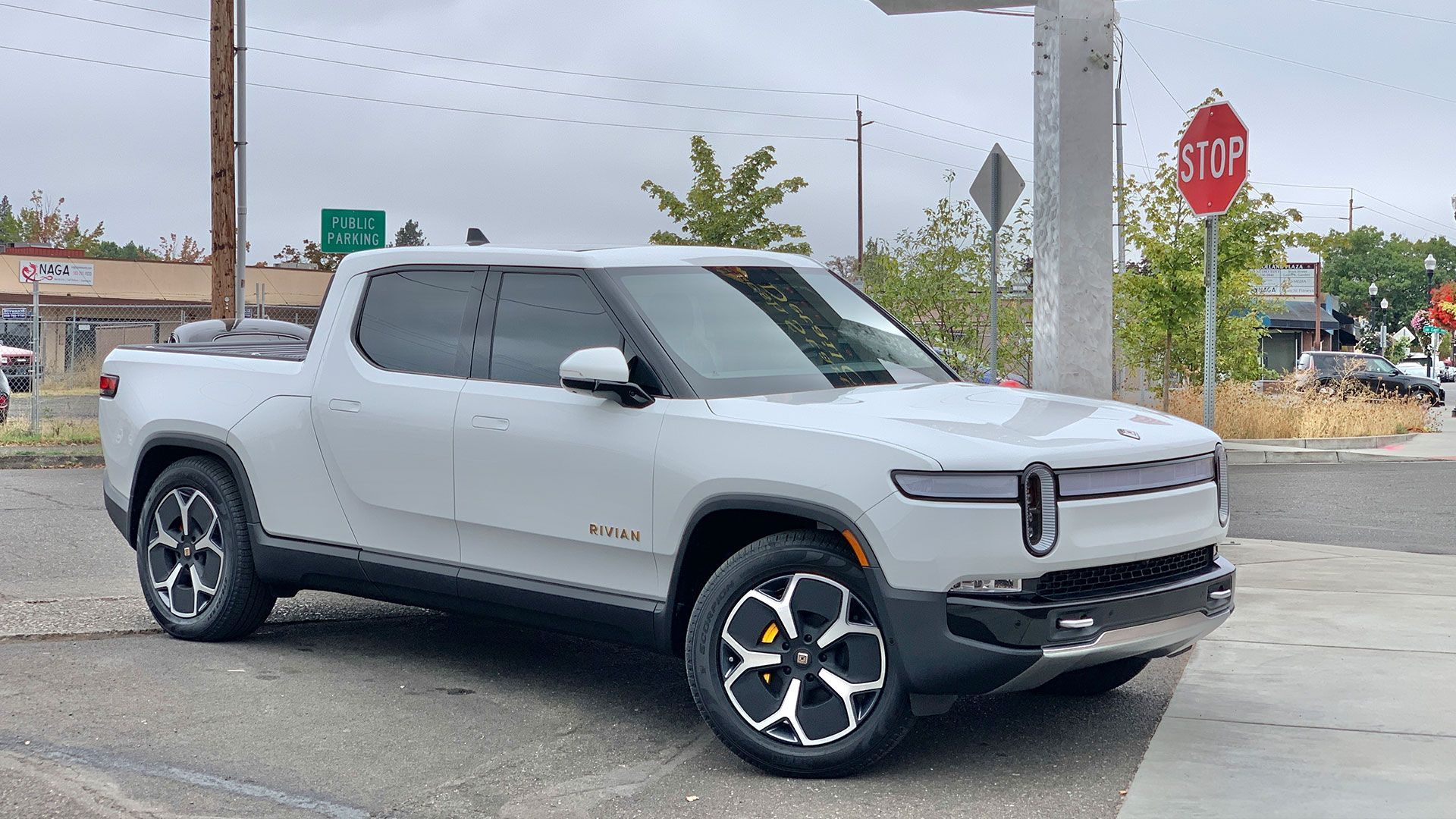 White Rivian pickup truck parked on a city street with a stop sign in the background.
