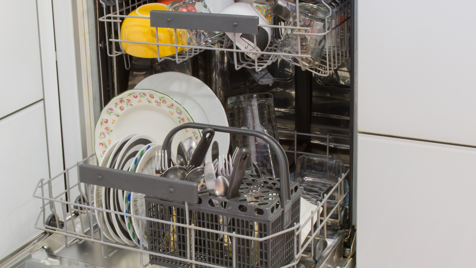 Dishwasher loaded with plates, cups, and silverware in a kitchen.
