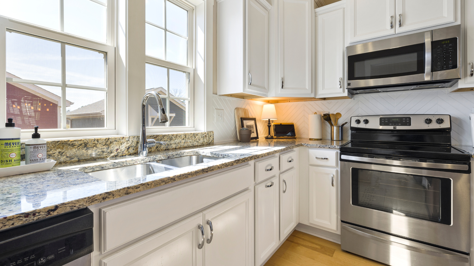 Bright white kitchen with stainless steel appliances, granite countertops, and a window above the sink.