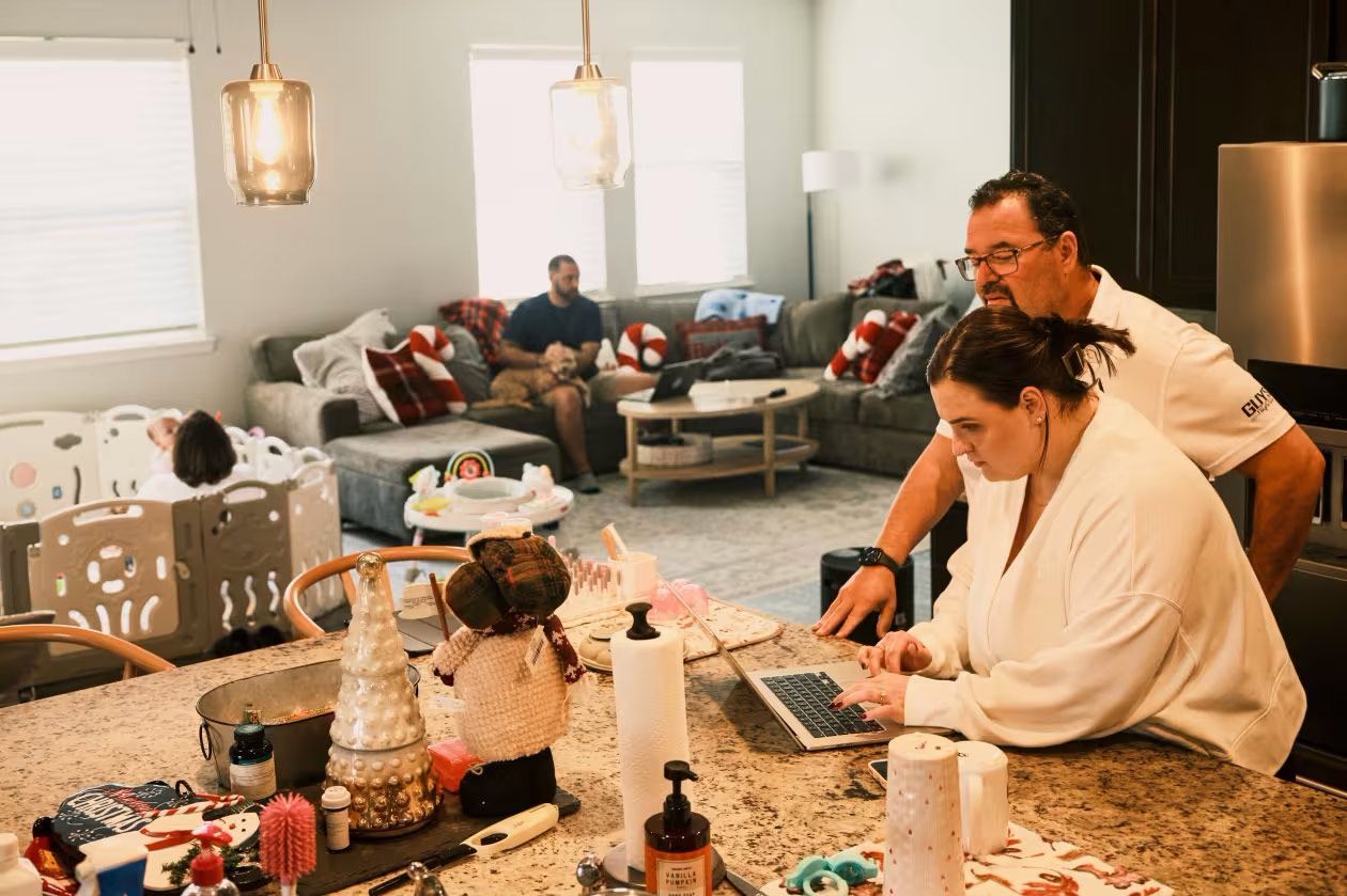 Gillian Held and her father, David, look over a laptop while Gillian’s mother, Cynthia, plays with 7-month-old Nora.