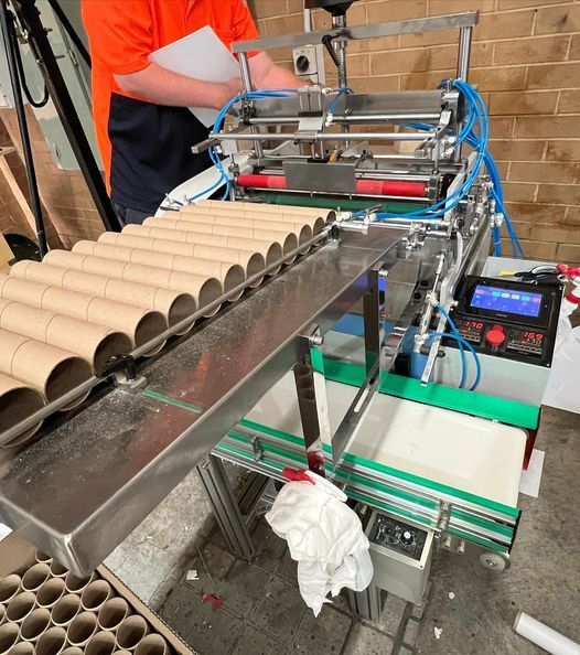 A man is working on a machine that is making toilet paper rolls