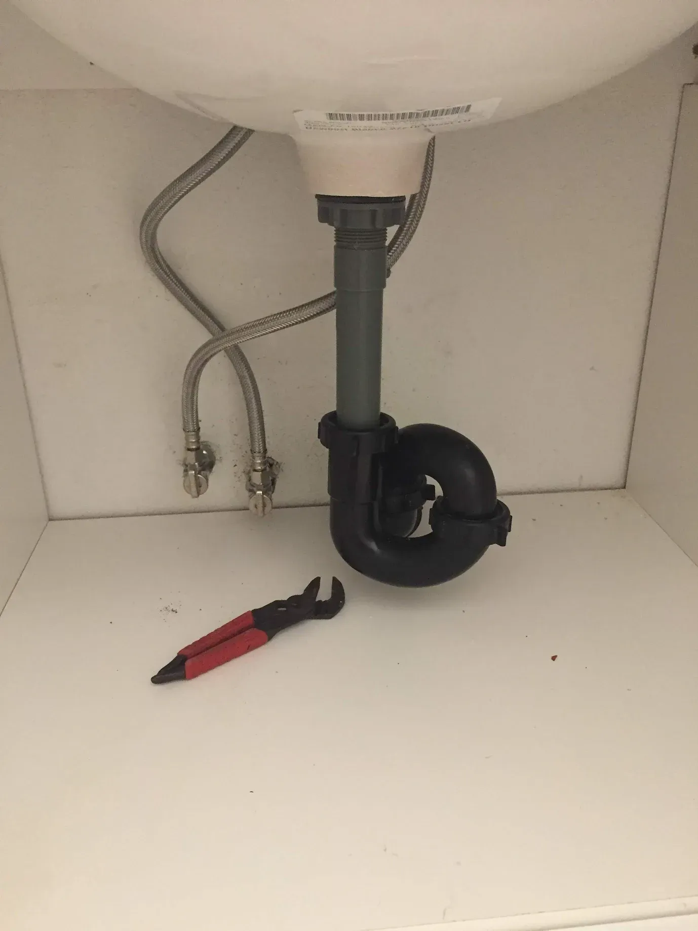 A sink with a black pipe underneath it and a wrench.