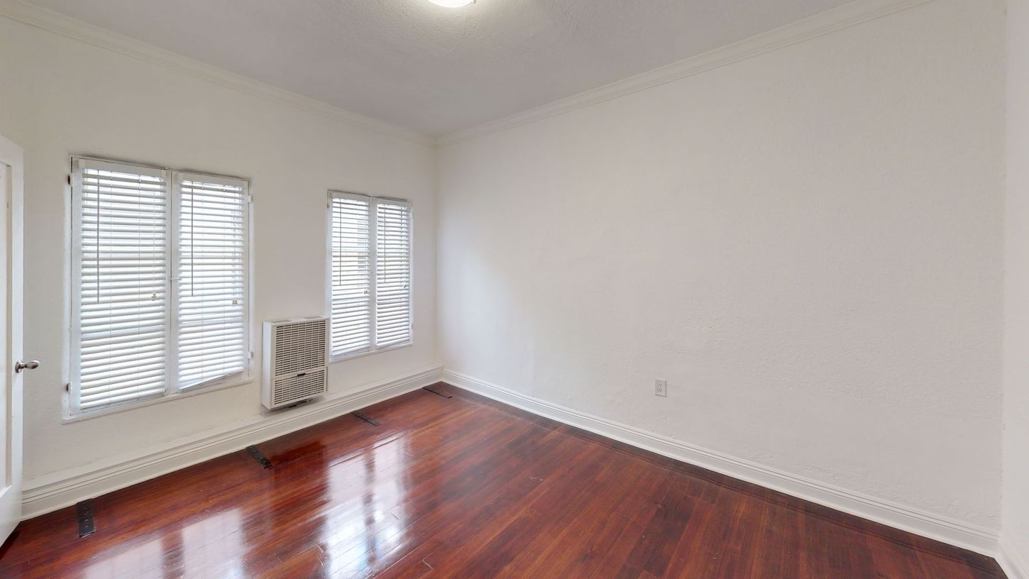 Empty room with wood floor, two windows with blinds, white walls, and a radiator.