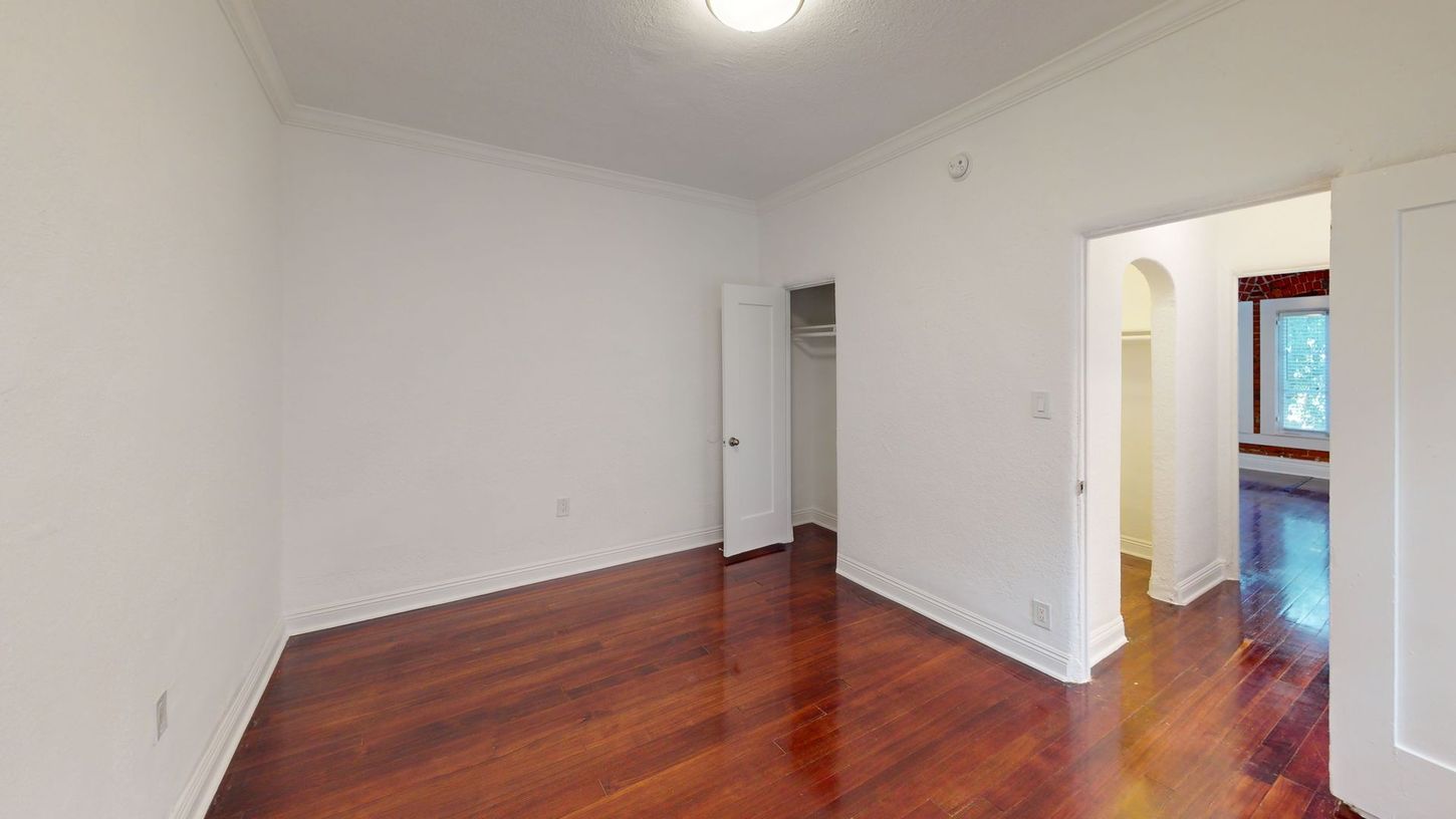 Empty room with wood floors and white walls. Doorways lead to a closet and another room.