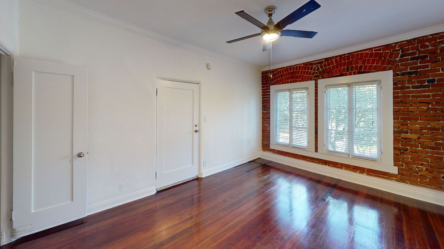 Empty room with hardwood floors, exposed brick wall, white doors, and windows.