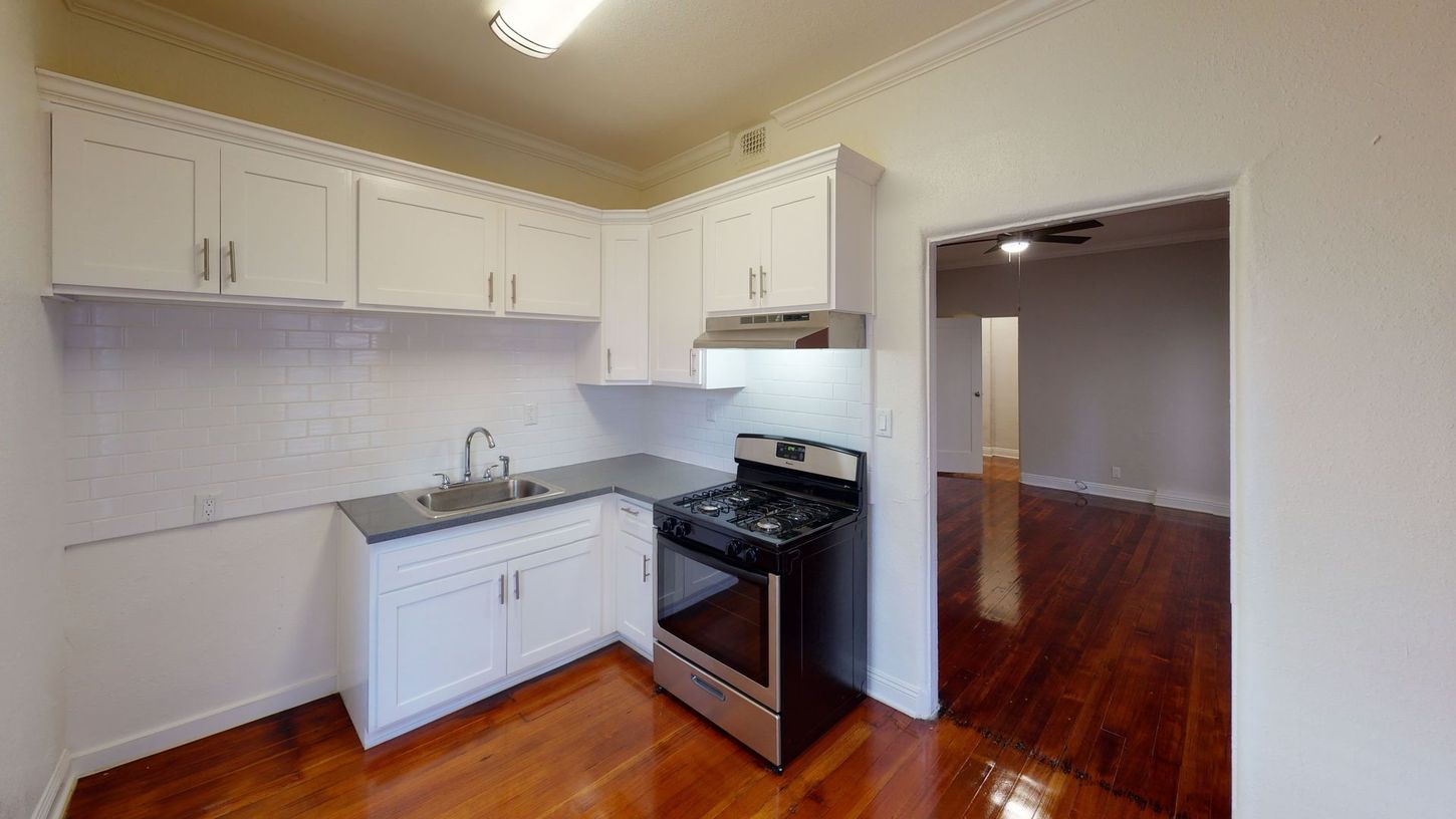 Narrow kitchen with white cabinets, stainless steel appliances, and wood floors.