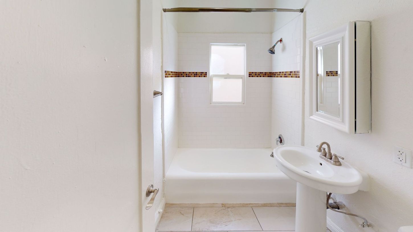 White bathroom with a pedestal sink, tub/shower, and small window.