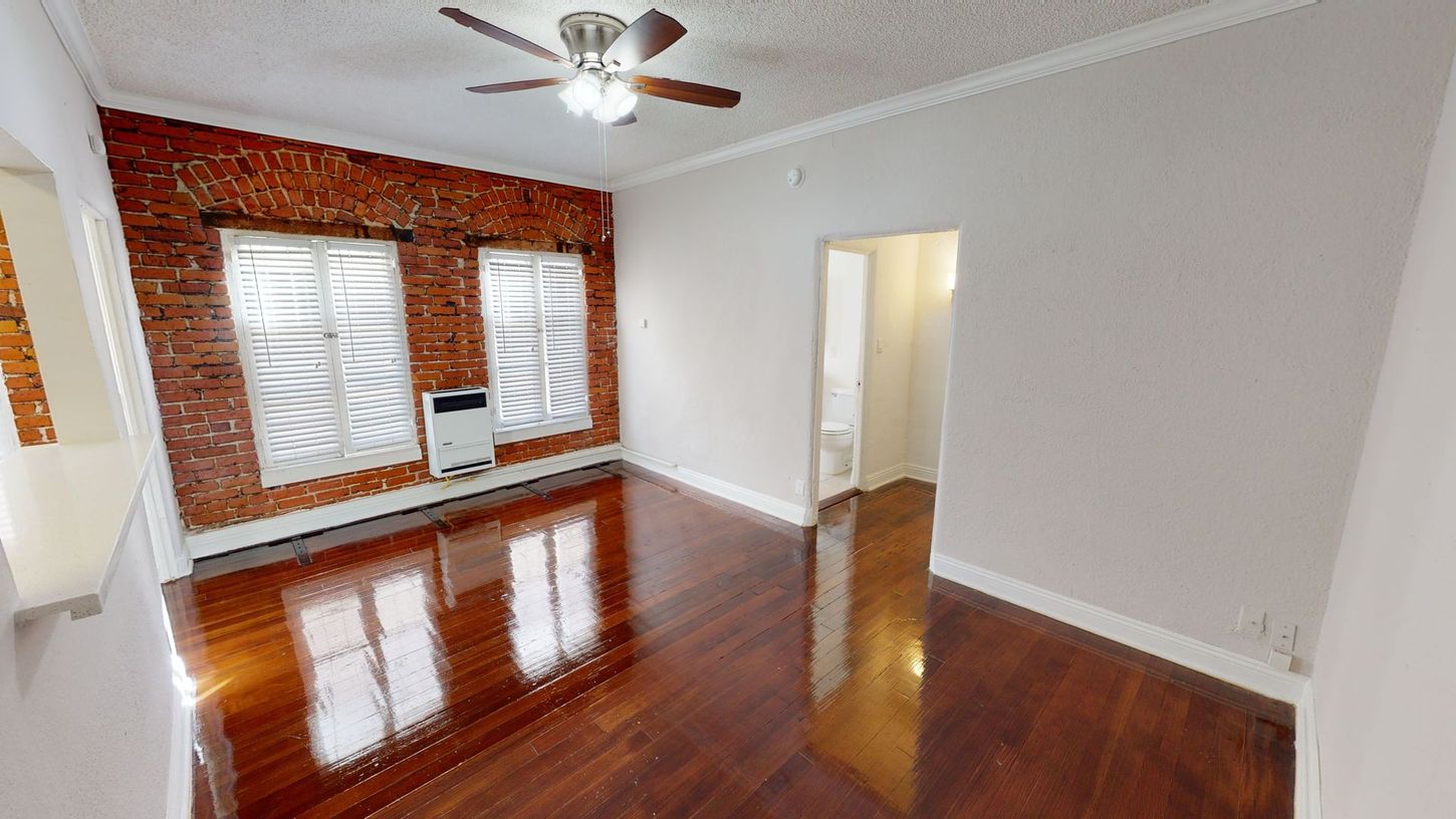 Living room with exposed brick wall, windows, and dark wood floors.