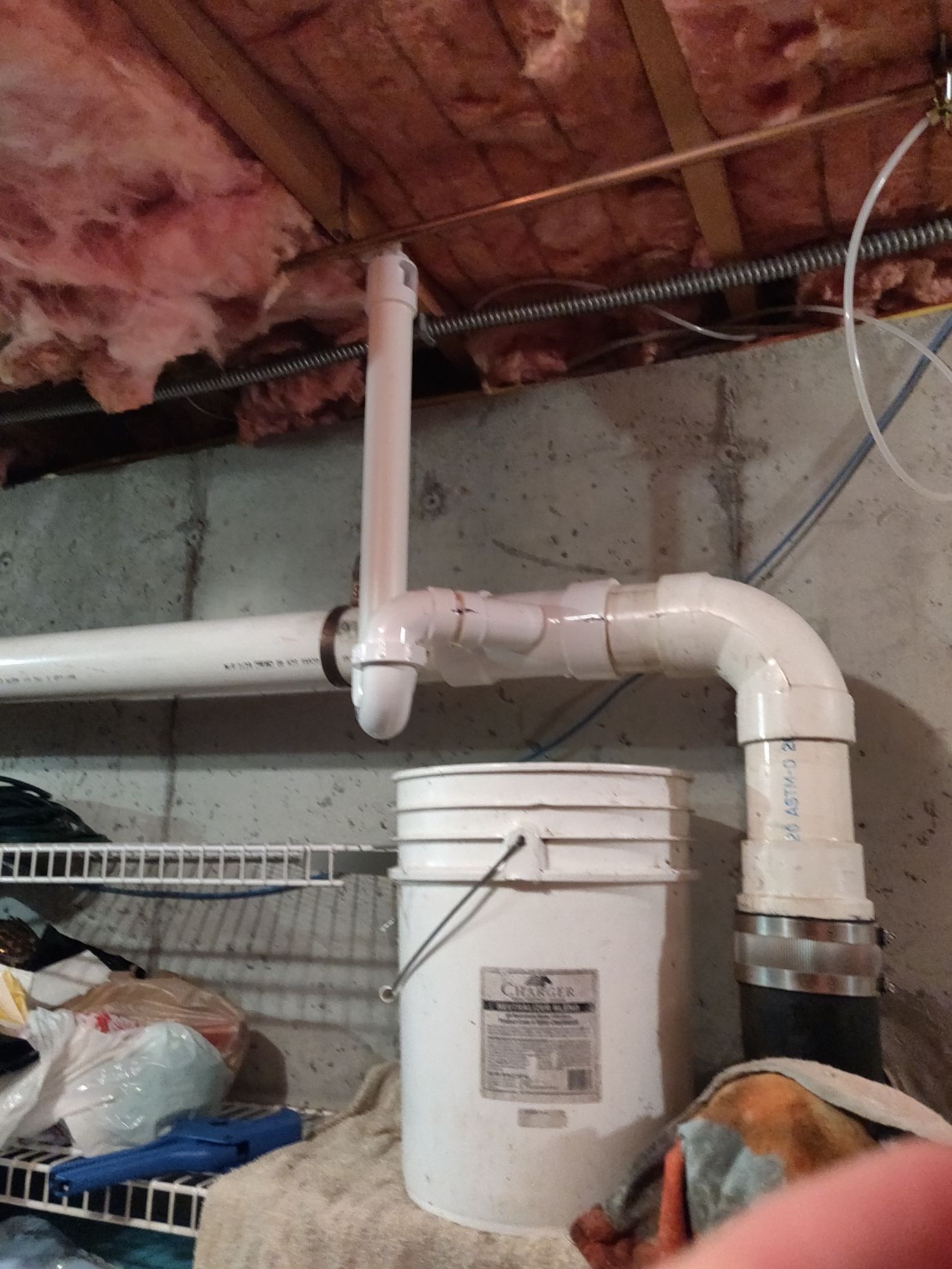 A white bucket is sitting next to a pipe in a basement.