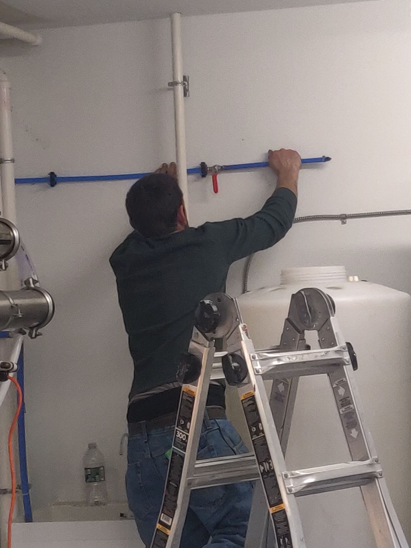 A man is standing on a ladder measuring a pipe on a wall.