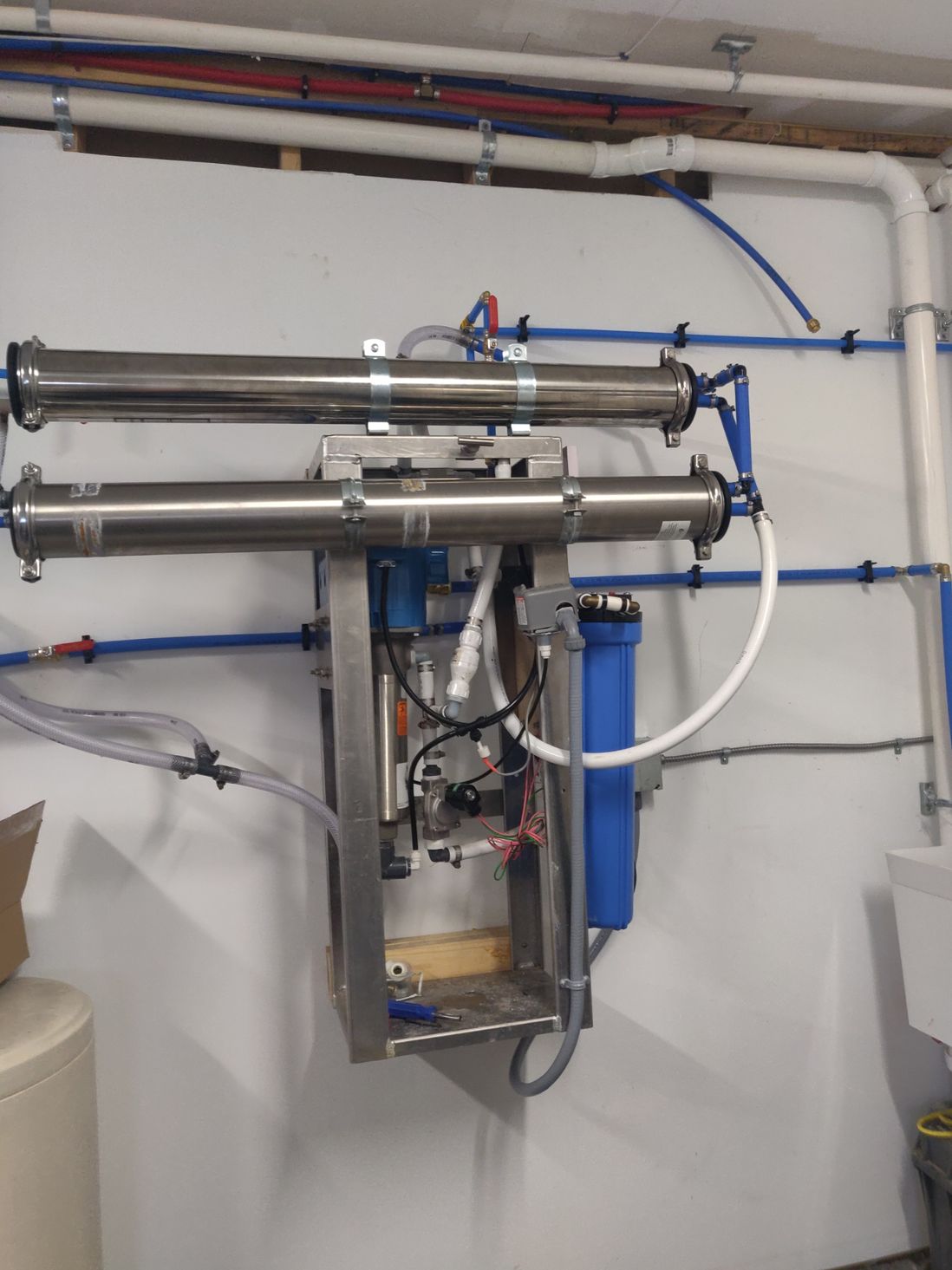 A stainless steel water filter is mounted to a wall.