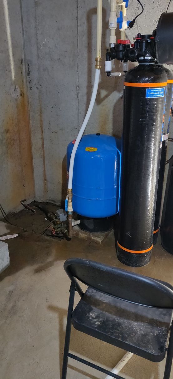 A water filter is sitting in a basement next to a chair.