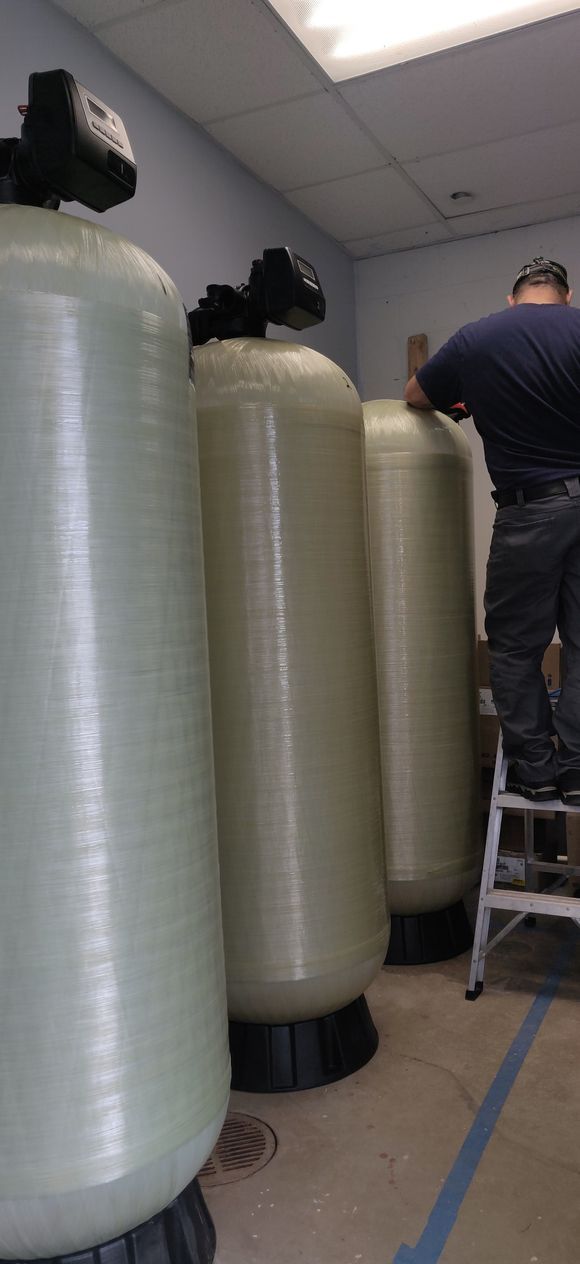 A man is standing on a ladder next to a row of water tanks.