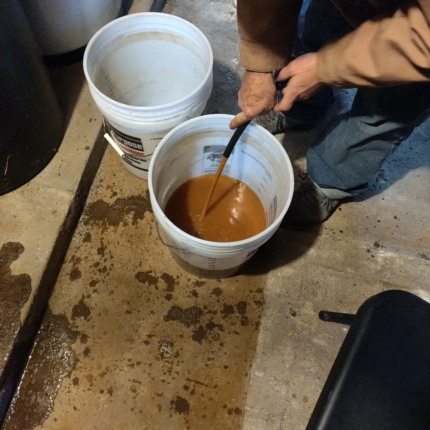 A person is mixing a brown liquid in a white bucket