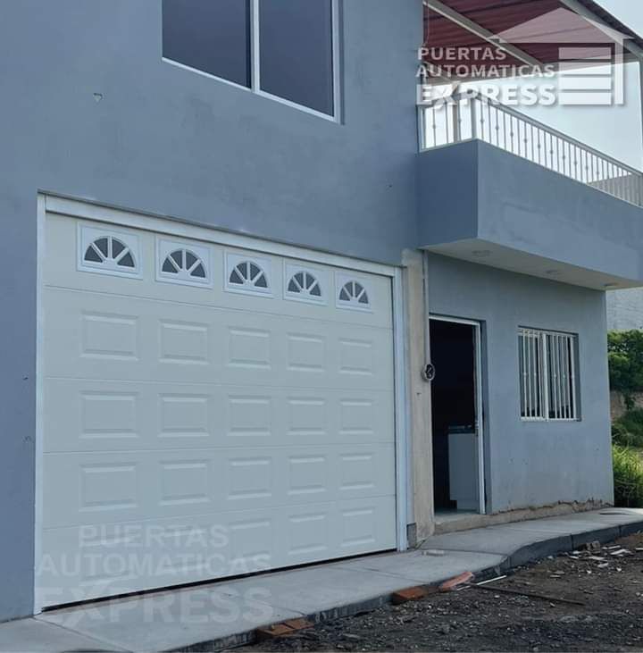 Puerta de garaje blanca en una casa azul claro con balcón y una pequeña ventana.