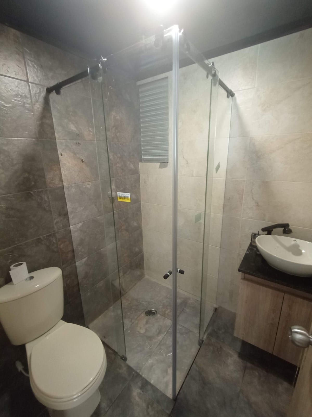 Baño con ducha de cristal, inodoro, tocador con lavabo blanco y paredes texturizadas.