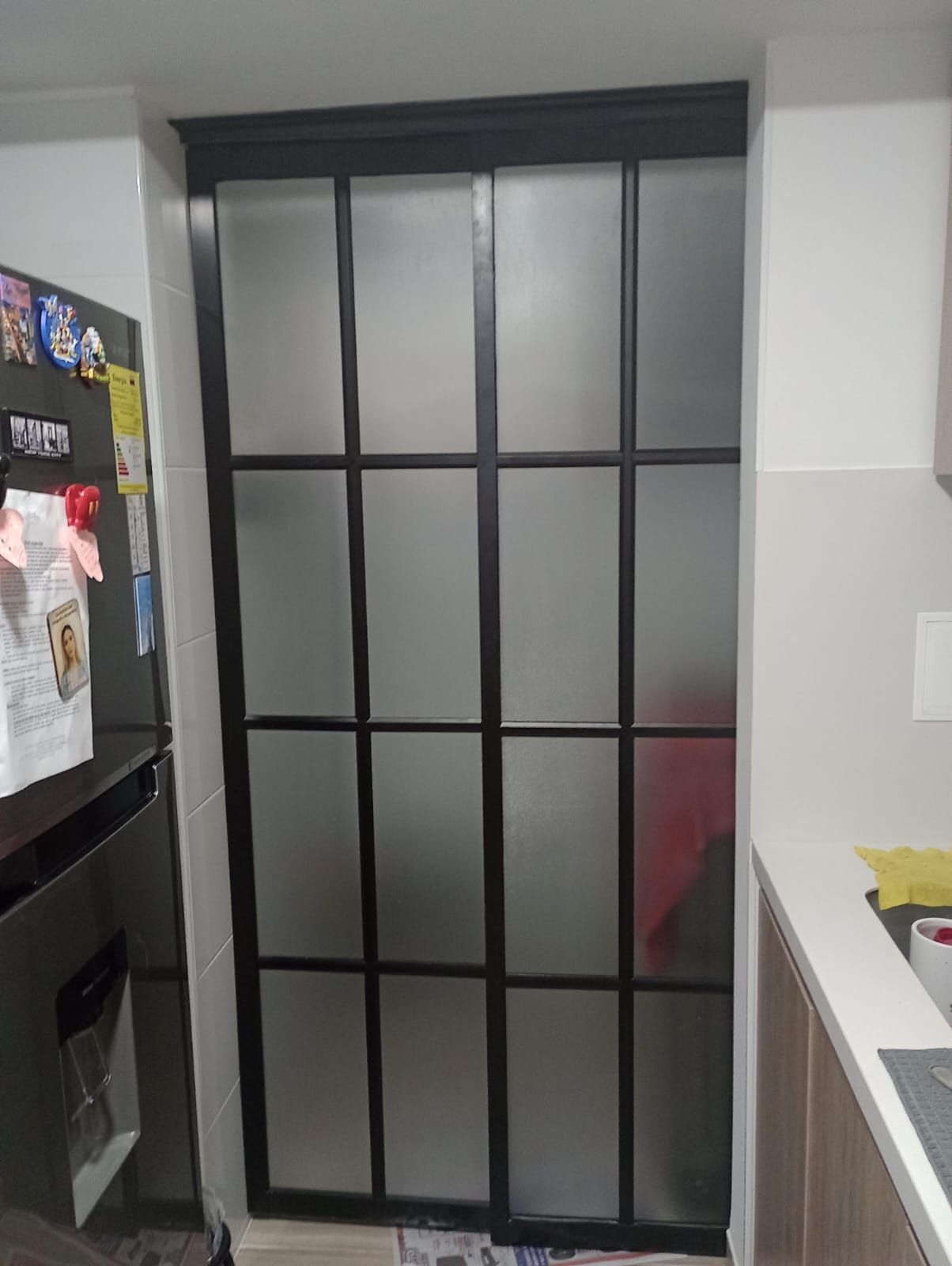 Puerta corrediza de vidrio esmerilado con marco negro en una cocina.