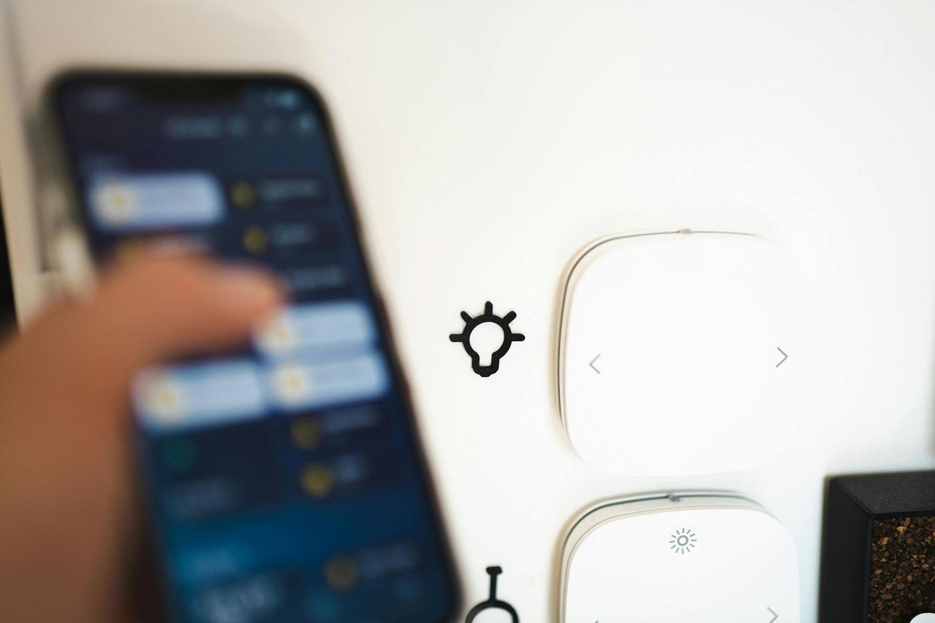 Blurred hand holding a smartphone near wall switches and a light control icon