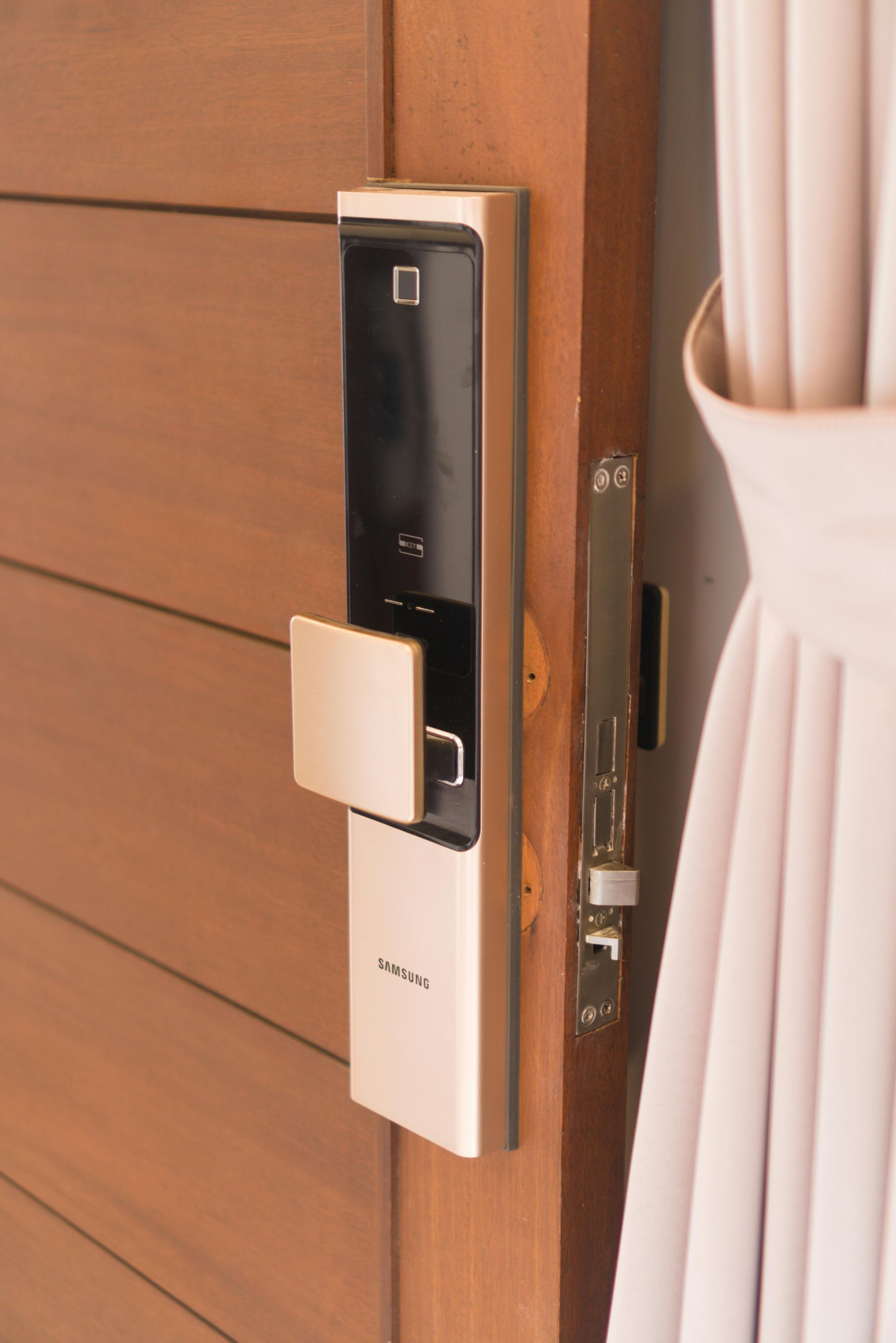 Digital door lock on a wooden door with a white curtain beside it