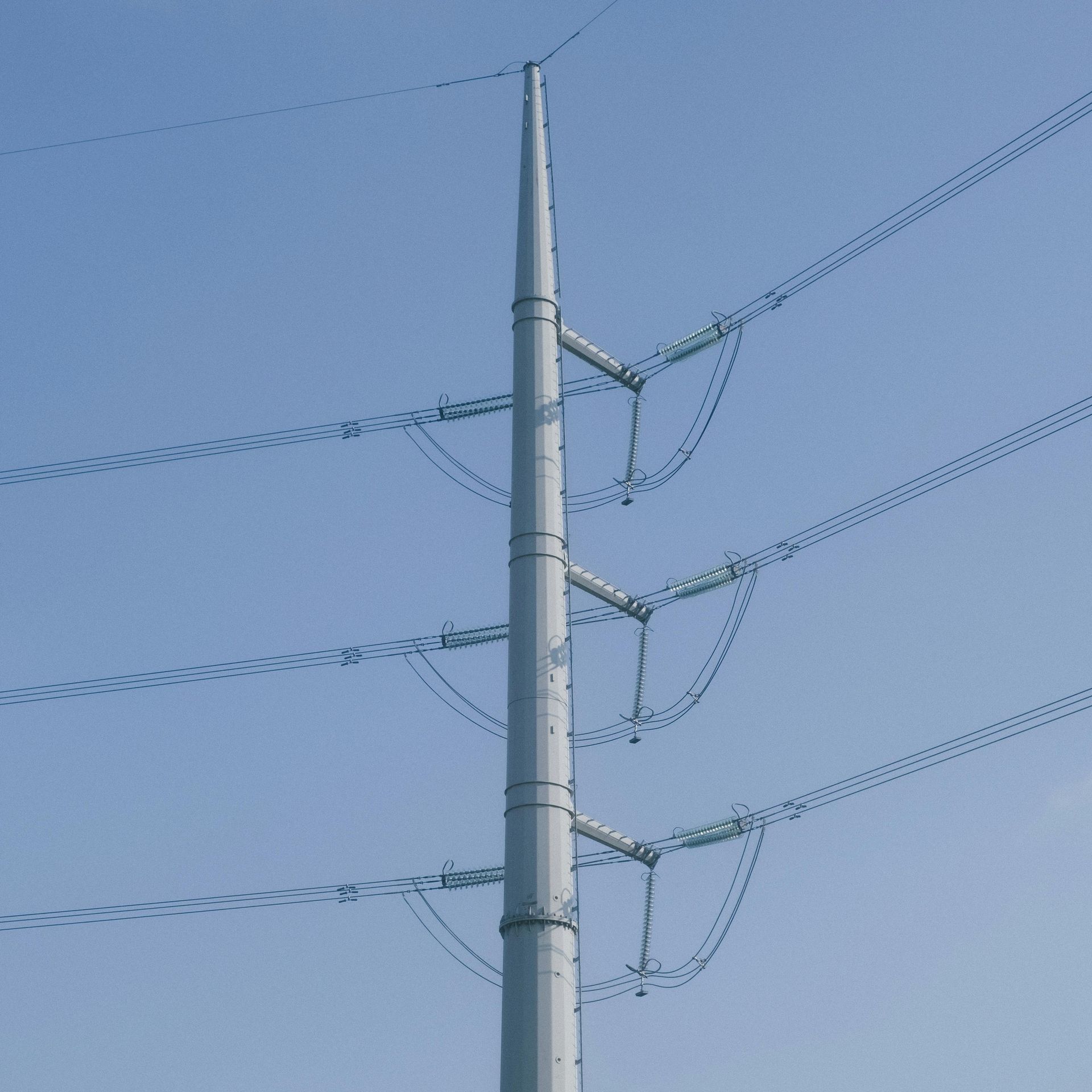 Utility pole with multiple power lines against a clear blue sky