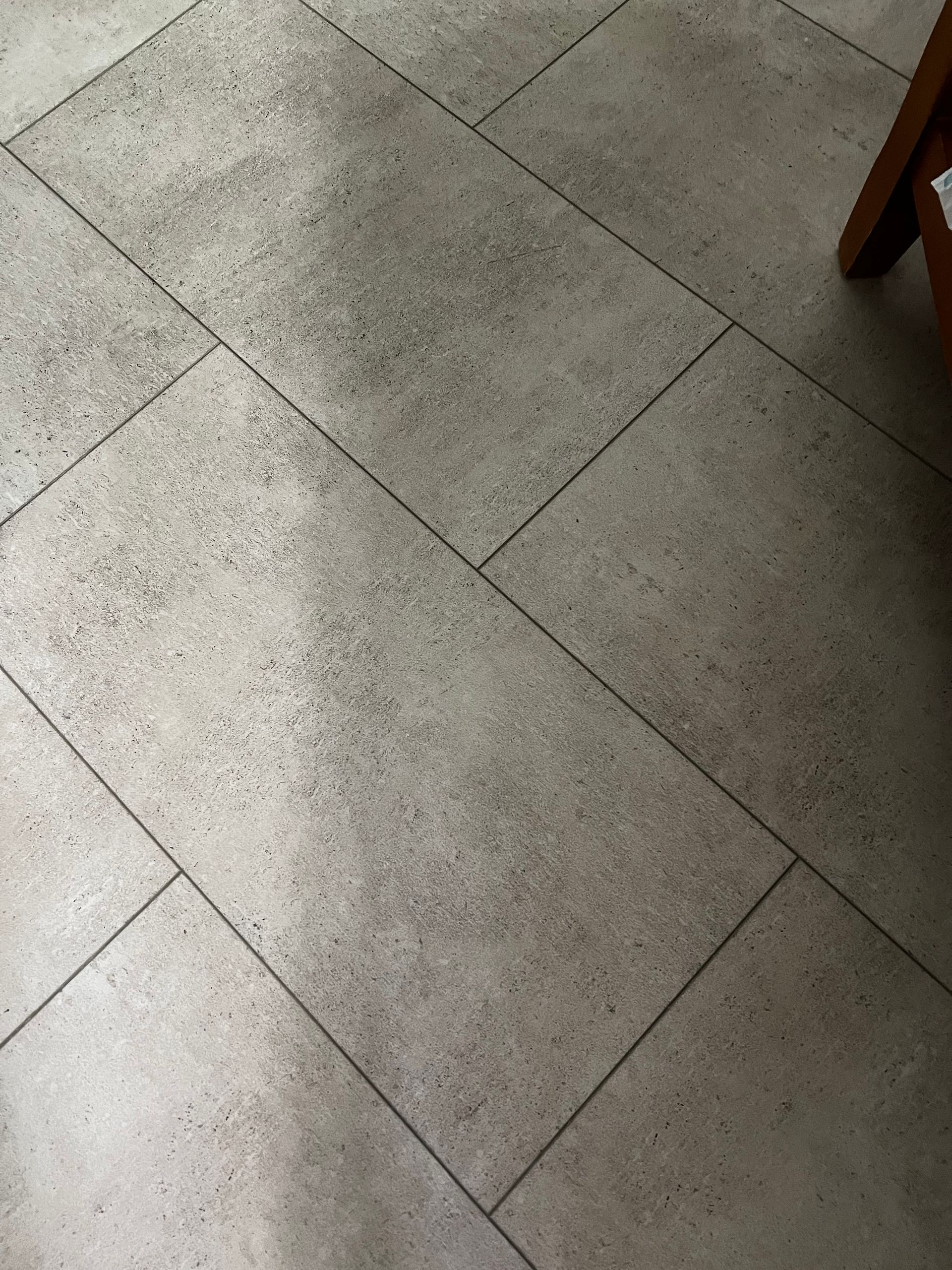 A close up of a tiled floor with a chair in the background.