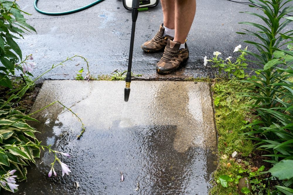 A person is using a high pressure washer to clean a sidewalk.