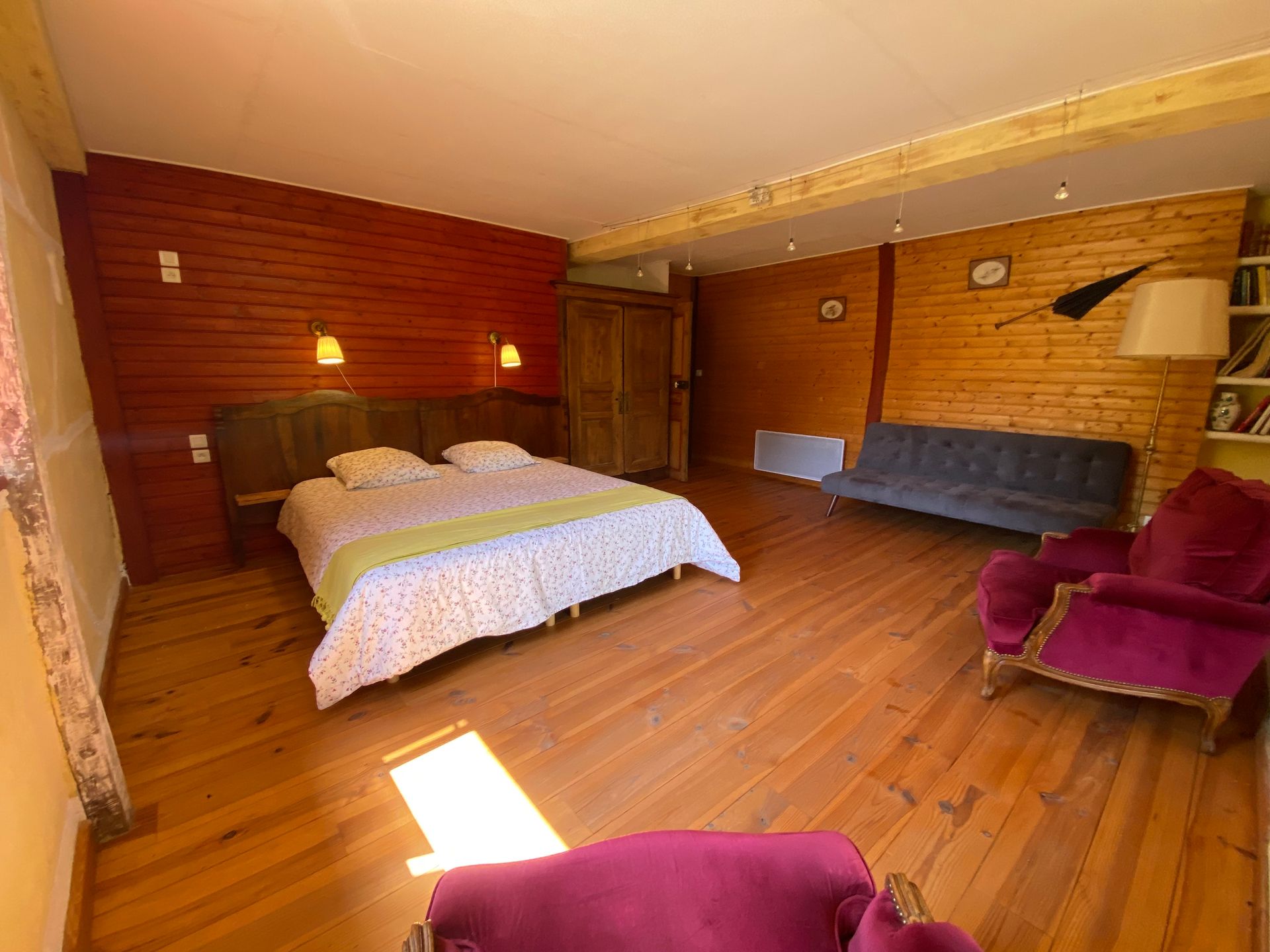 Chambre avec parquet et murs en bois, comprenant un lit, un canapé, un fauteuil et une bibliothèque.