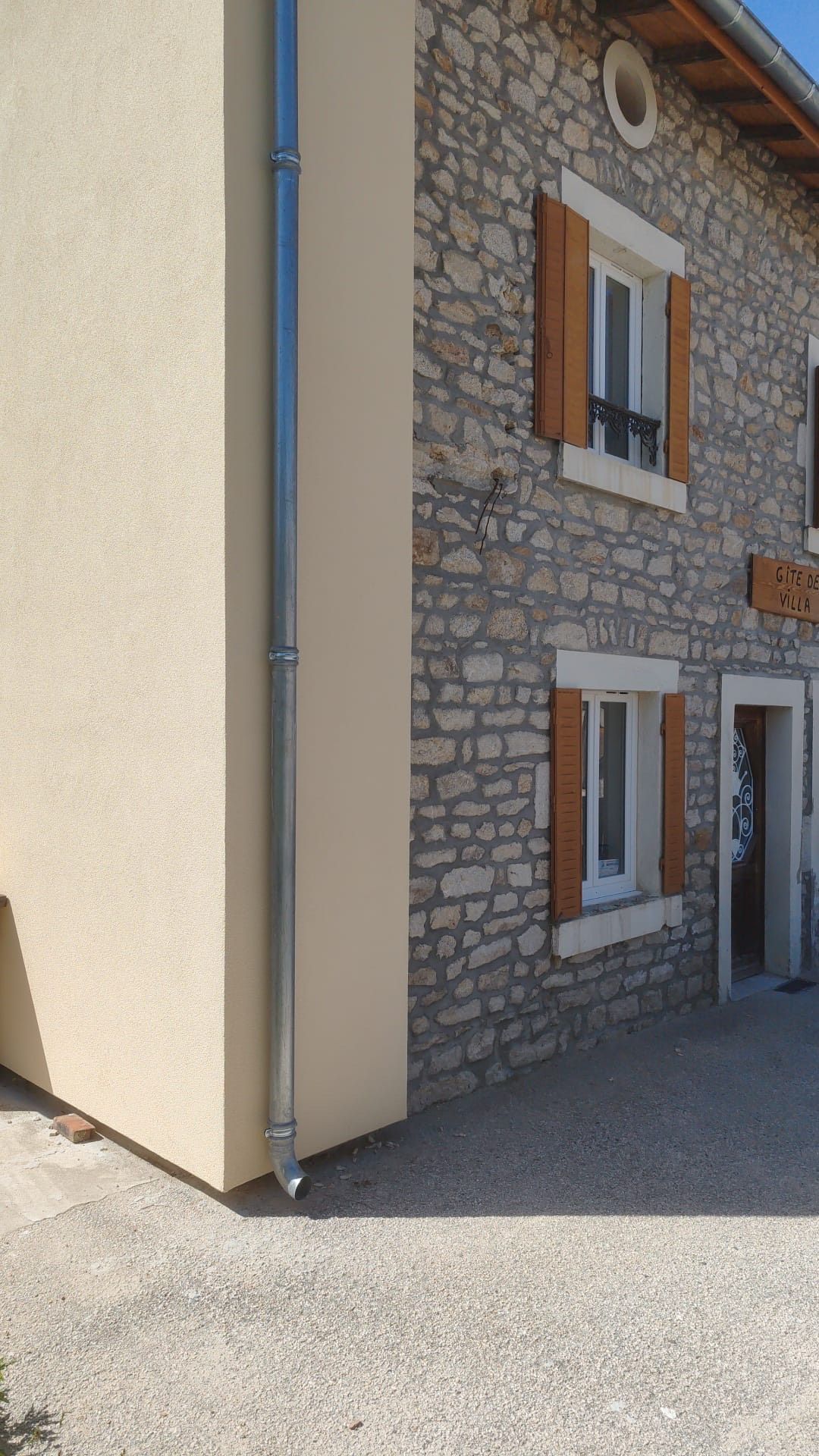 Vue extérieure d'un bâtiment en pierre de deux étages avec des volets beige clair et un mur en stuc beige clair. 