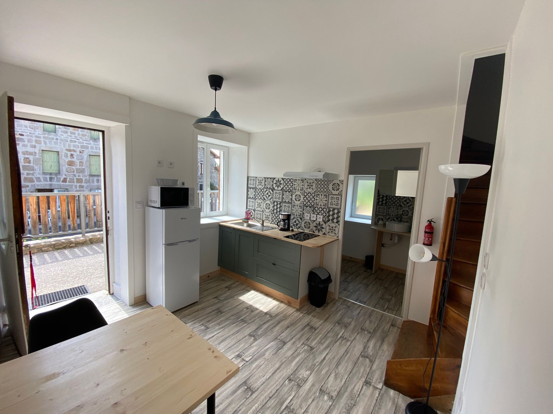 Vue intérieure d'une petite cuisine et salle à manger avec un réfrigérateur, un micro-ondes et une porte menant à un balcon.