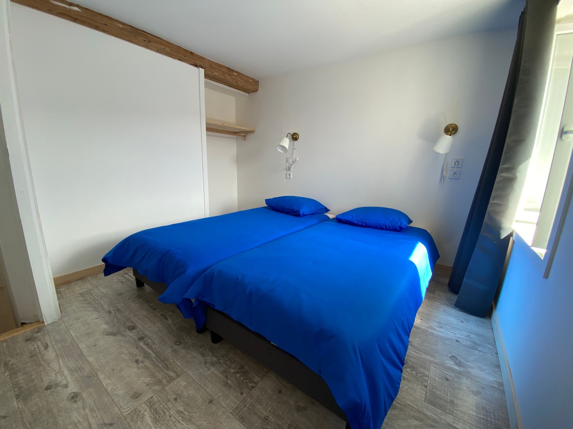 Une chambre avec deux lits jumeaux recouverts de linge de lit bleu. Elle est équipée d'appliques murales.