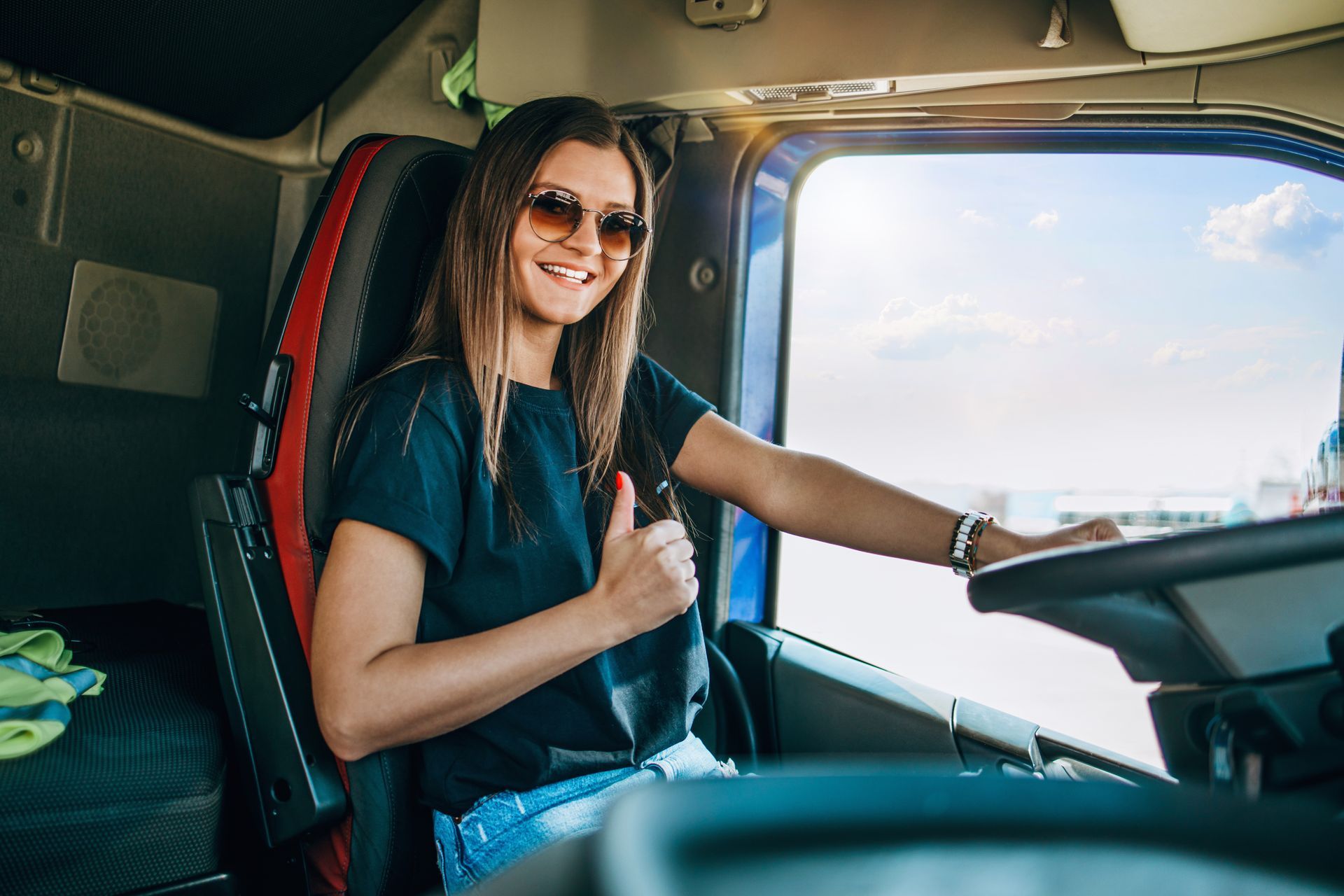 A woman is sitting in the driver 's seat of a truck and giving a thumbs up.
