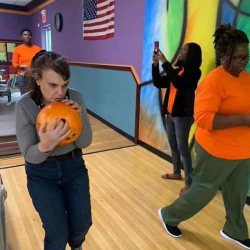 Developmentally disabled individual joyfully attempts bowling with support from Direct Support Professionals (DSP)