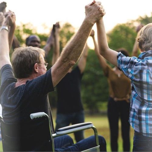 Group of elderly and disabled individuals joyfully holding hands high, symbolizing unity and support in community-integrated programs.