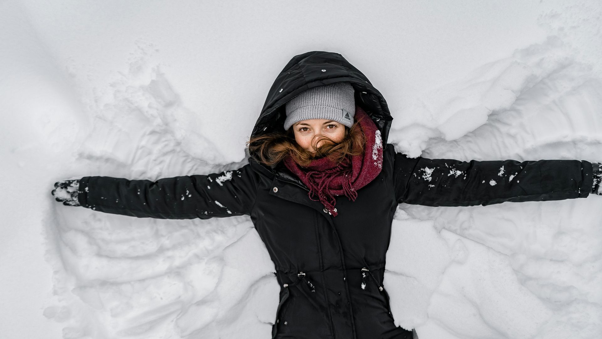 Woman wearing jacket laid down in snow in a playful manner