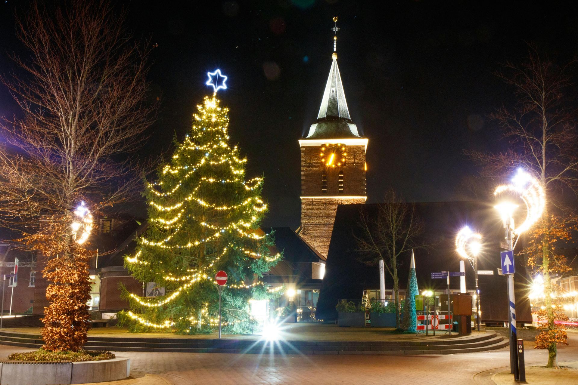 Festive town center at night, featuring strings of holiday lights and large Christmas decorations.