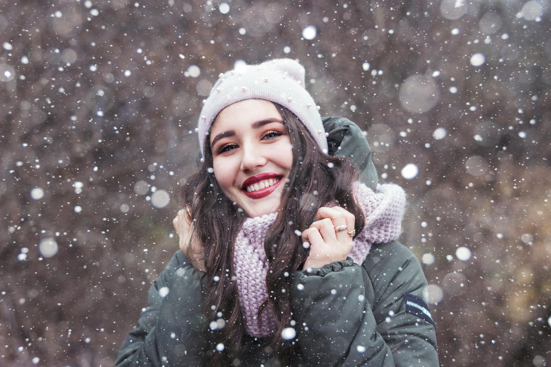 Smiling woman wearing warm clothing while standing in snow, expressing warmth and positivity.