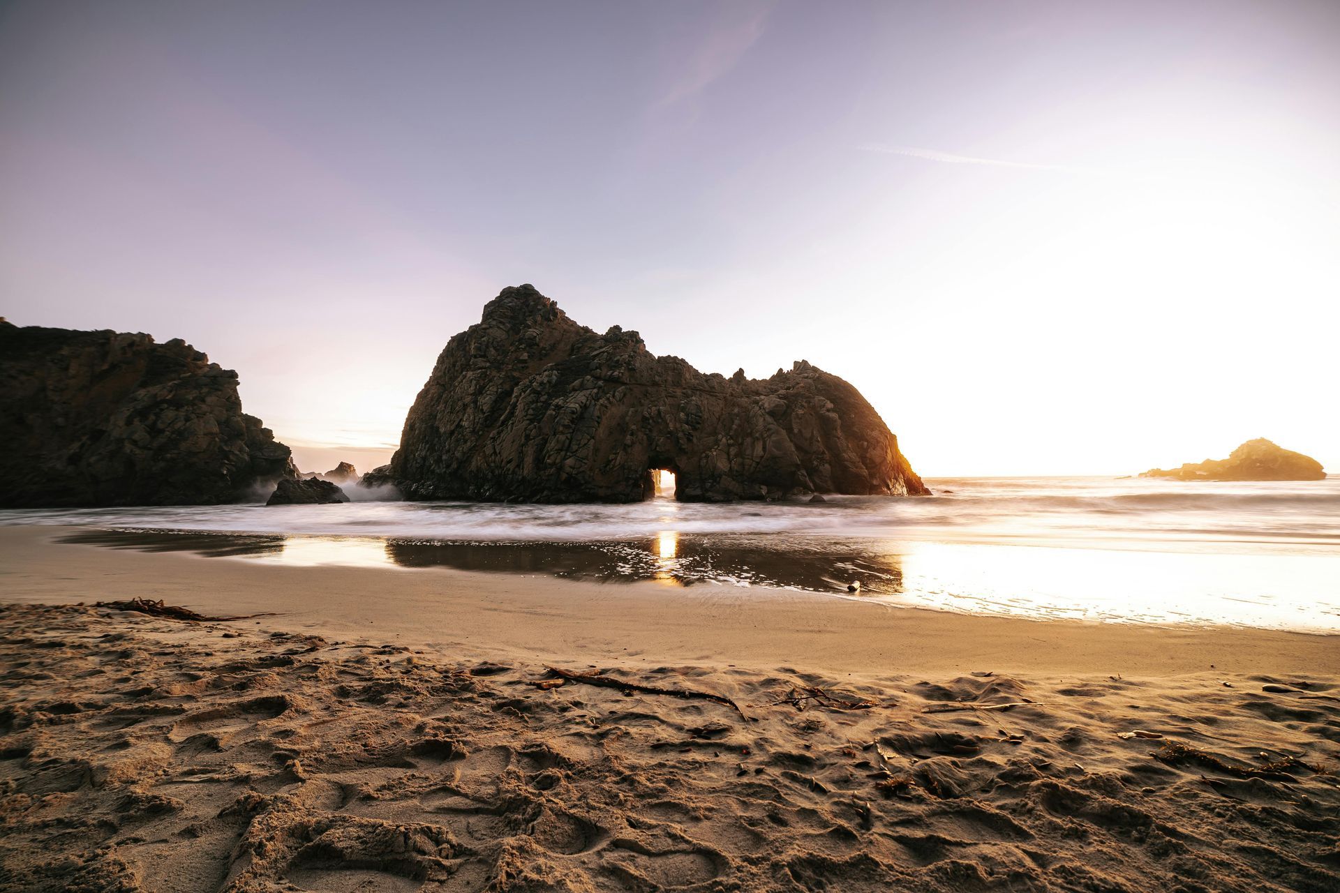 Sea meeting shoreline at sunset with mountains in background, creating a peaceful & reflective scene