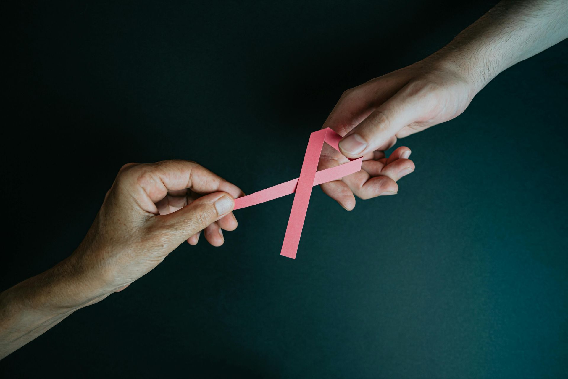 2 hands holding a pink ribbon