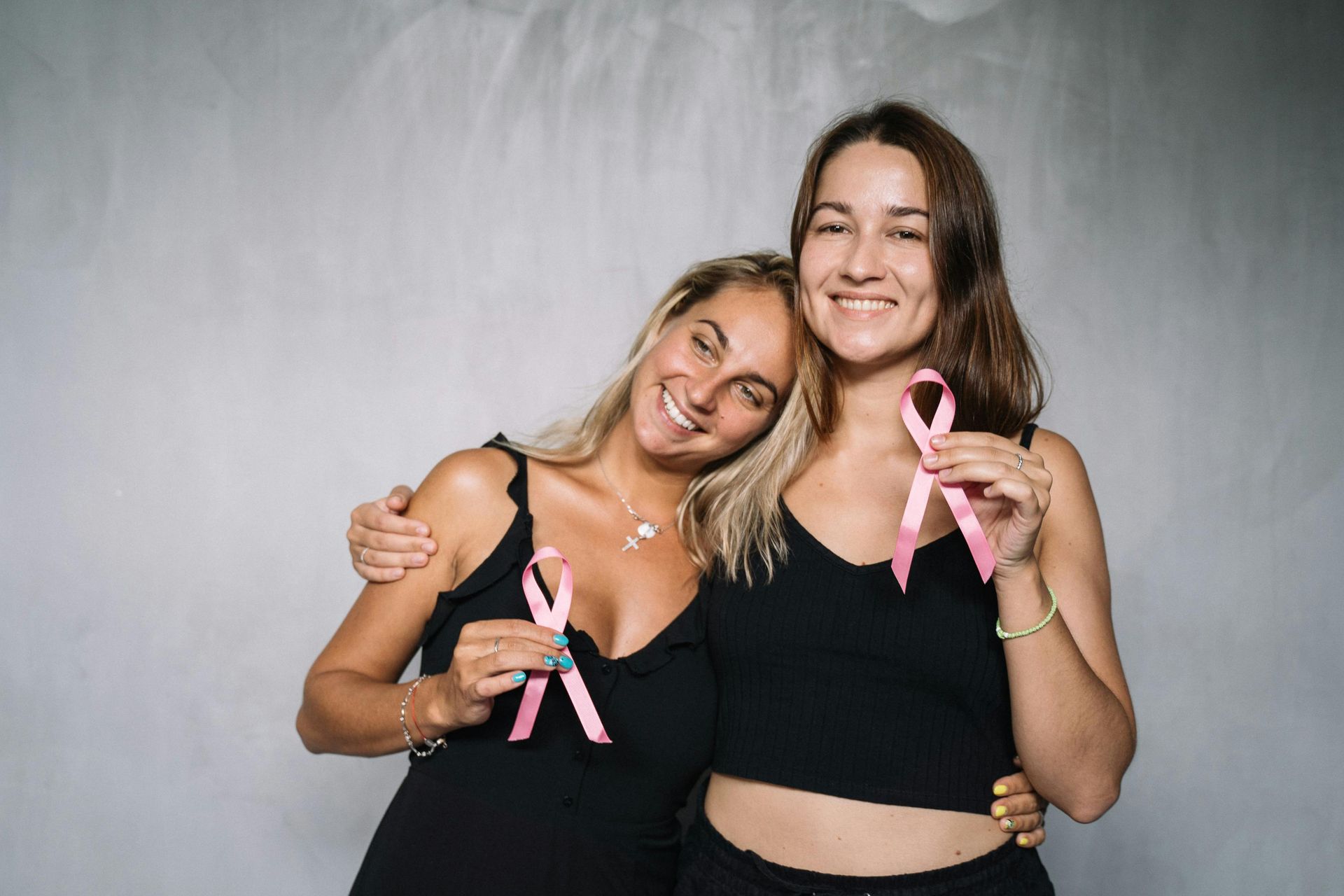 2 women holding pink ribbons in support of breast cancer awareness