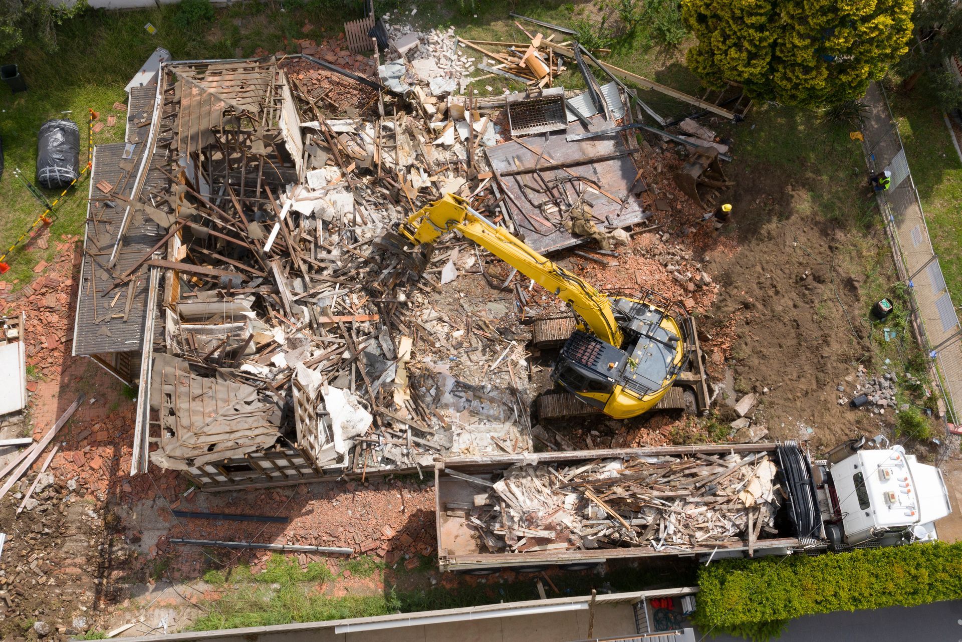 Demolition of a house, yellow excavator, debris pile, truck, overhead view.
