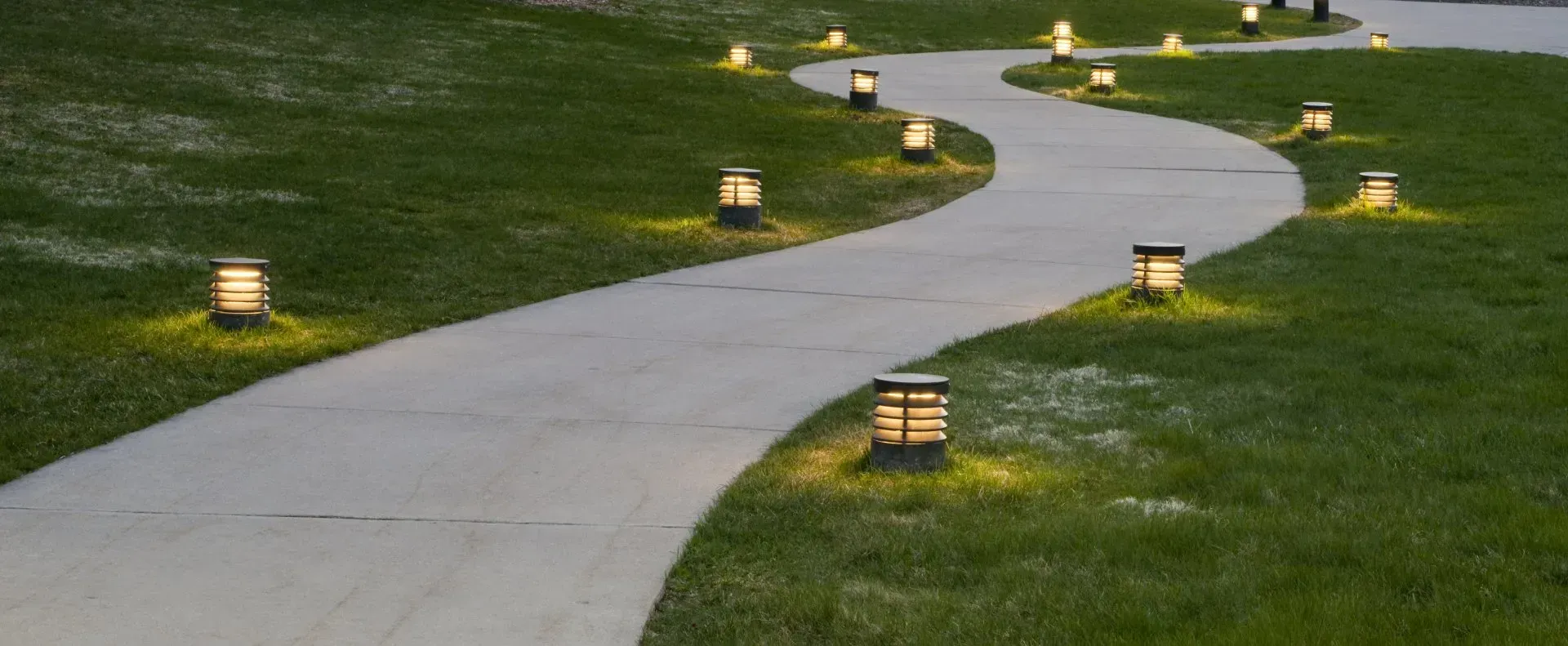 A winding pathway illuminated by small, glowing lights in a grassy outdoor setting.