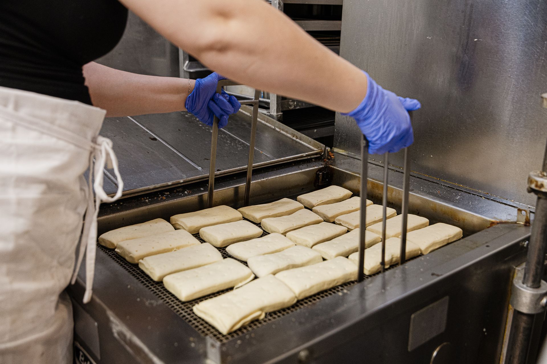 A golden-brown pastry topped with thick orange frosting and a crumbly streusel topping, held in white paper.