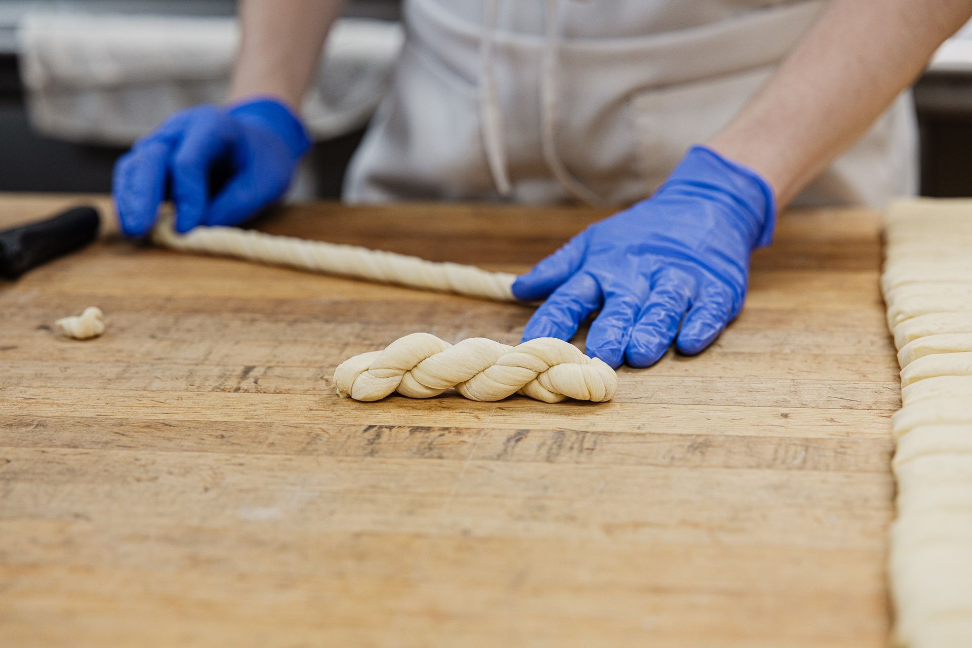 A batch of golden-brown braided pastries topped with dollops of white cream, displayed in a clear container.