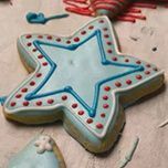 A star-shaped sugar cookie with light blue icing, a blue piped outline, and a row of small red dots on parchment paper.
