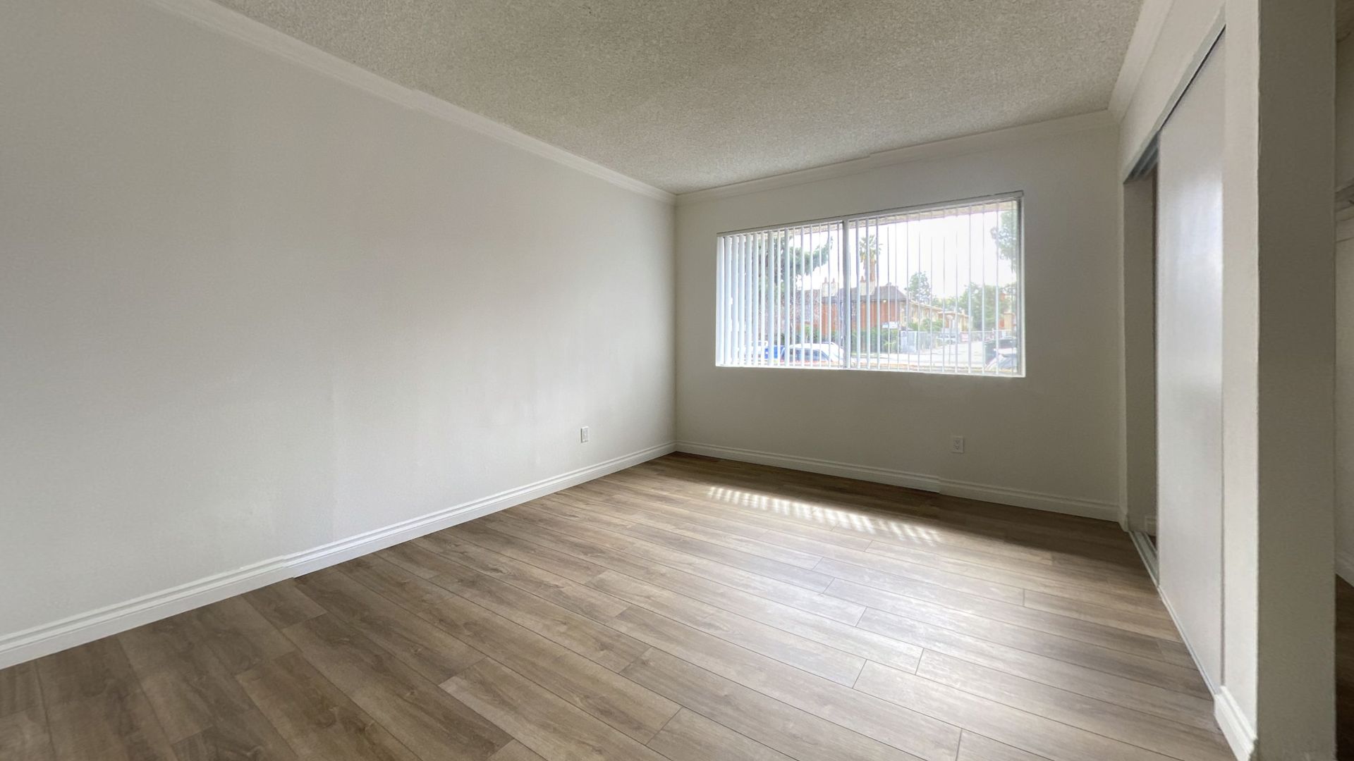 Empty room with wood-look flooring, white walls, a window, and a sliding closet door.