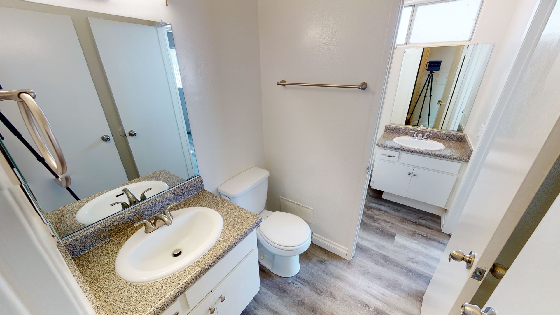 Bathroom with a vanity, toilet, and a doorway to another room. Neutral colors, natural light.
