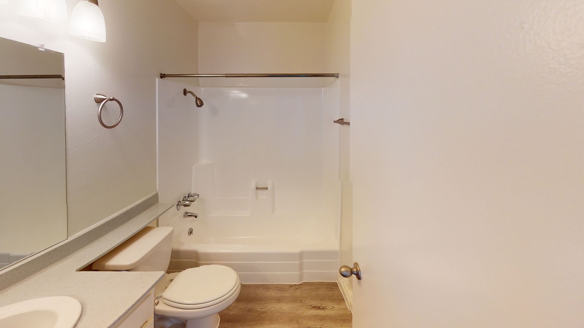 Bathroom with a white bathtub, toilet, and sink. Beige walls and brown flooring.