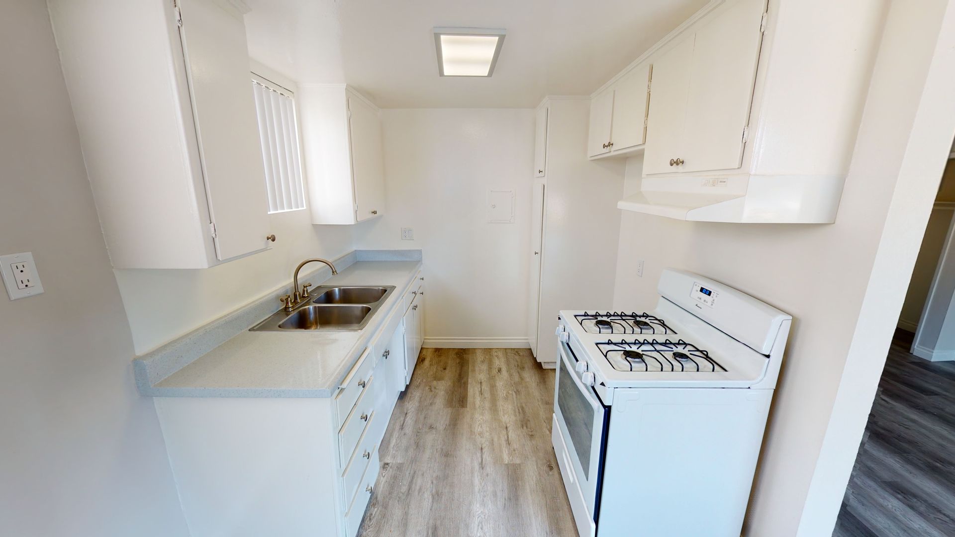 White kitchen with cabinets, stove, and sink. Light wood-look flooring.